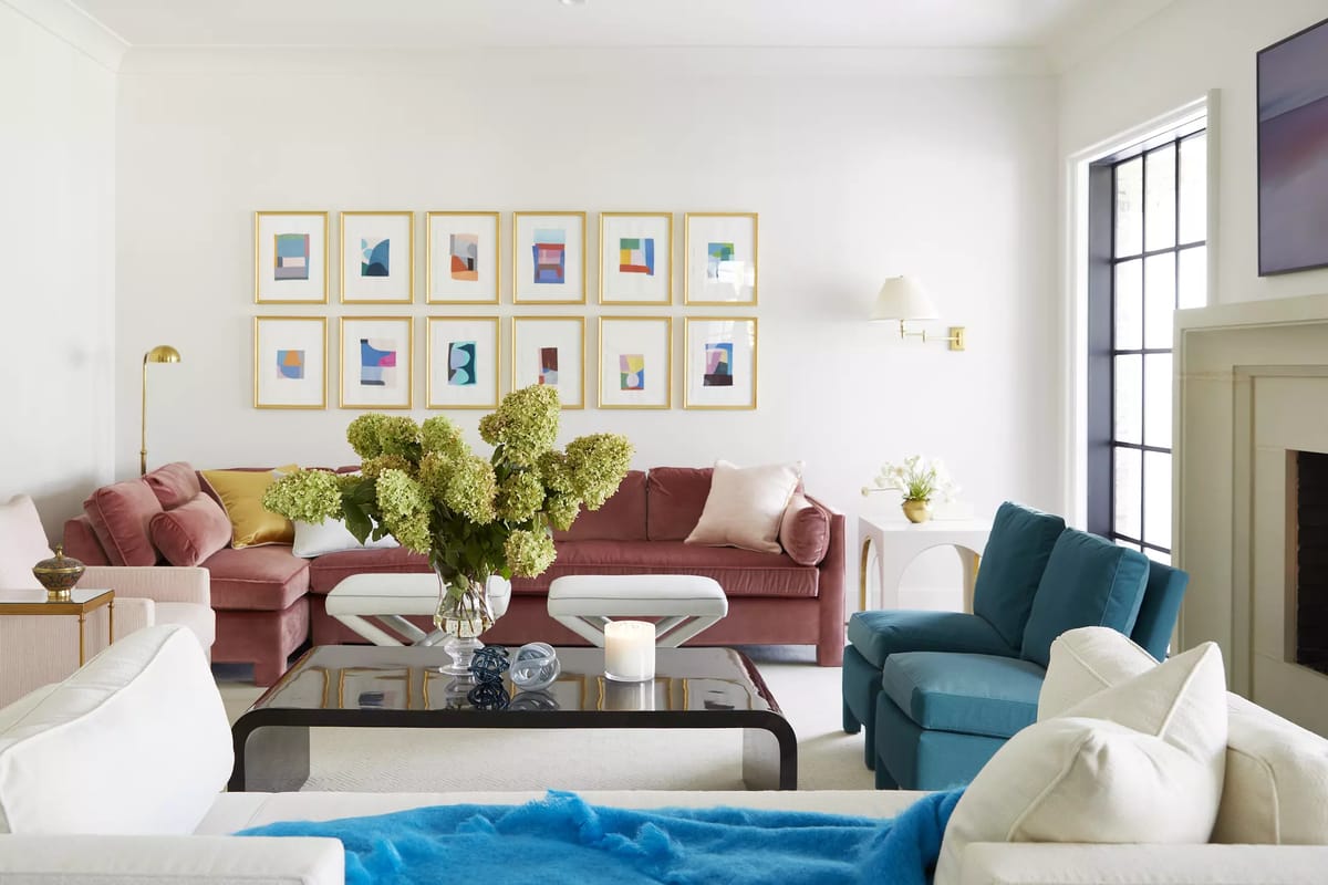 Living room with pink and teal sofas, glass coffee table, artwork, floral arrangement, and fireplace.