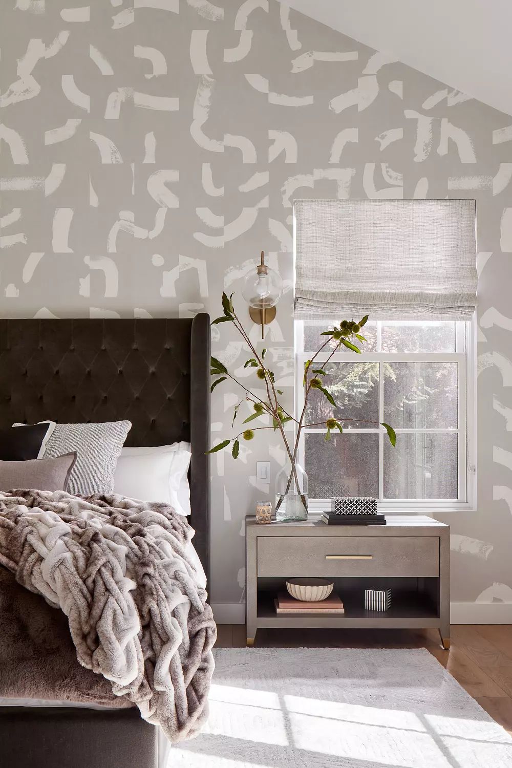 Bedroom with tufted bed, brown throw blanket, bedside table, decorative vase, and patterned wallpaper