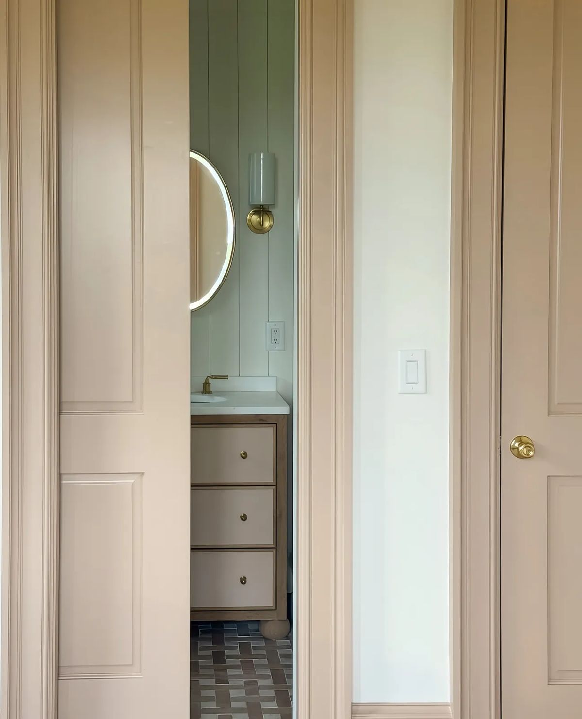 Bathroom with beige paneled walls, round mirror, white vanity, and tiled floor.