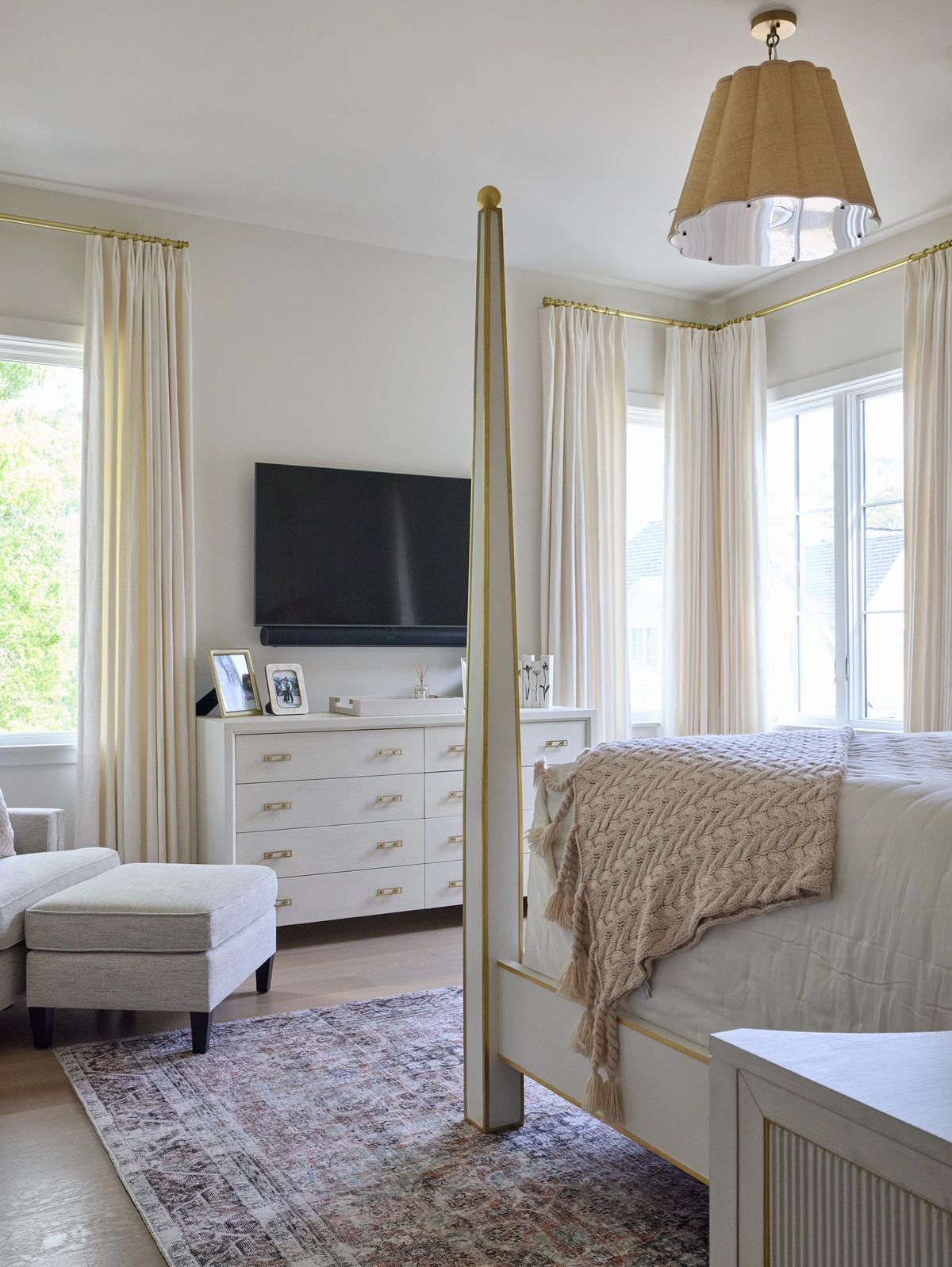 Bedroom with canopy bed, beige throw, nightstands, armchair, and vintage area rug with large windows