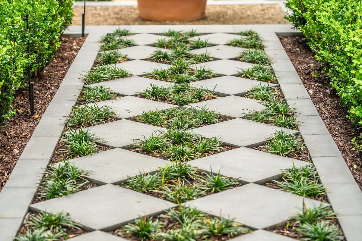 Garden pathway with diamond-shaped pavers and green grass between low hedges.