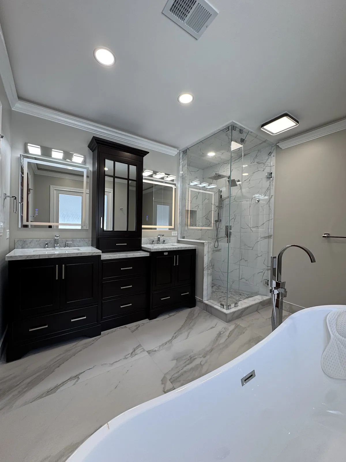 Bathroom with glass shower, freestanding bathtub, dark wood vanity, and marble flooring.