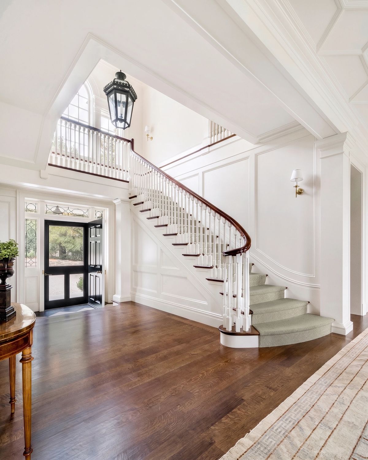 Foyer with curved staircase, hardwood floor, wall paneling, and decorative lantern.