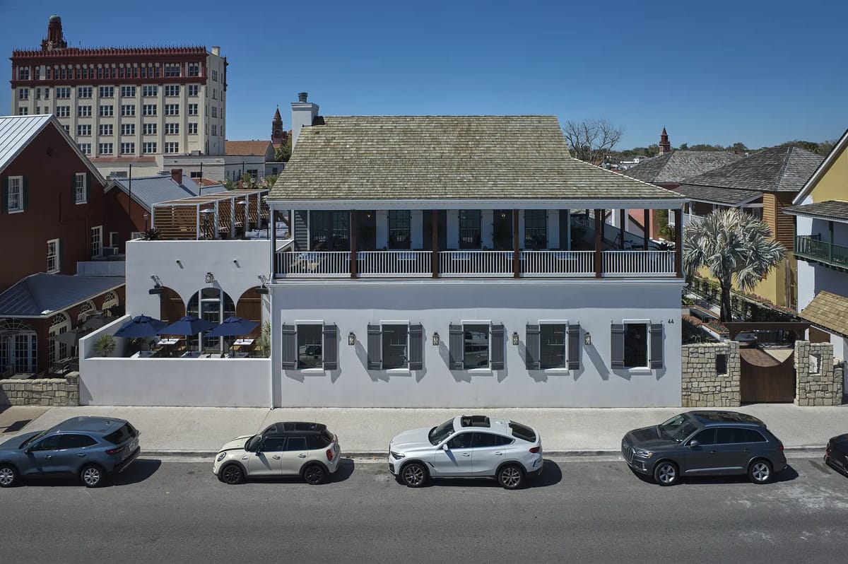 Two-story building with sloped roof, windows, deck, and parked cars along the street.