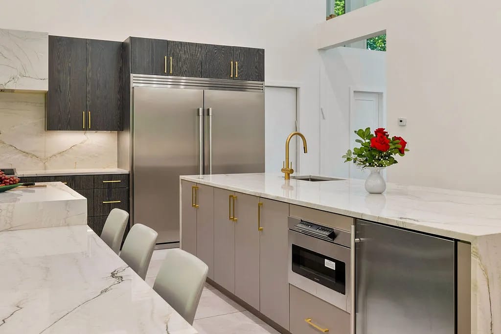 Kitchen with dark cabinetry, stainless steel appliances, white marble countertops, and bar stools.