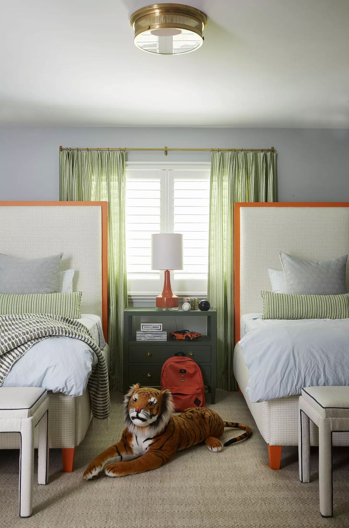 Bedroom with twin beds, green curtains, nightstand, table lamp, plush tiger toy, and backpack.