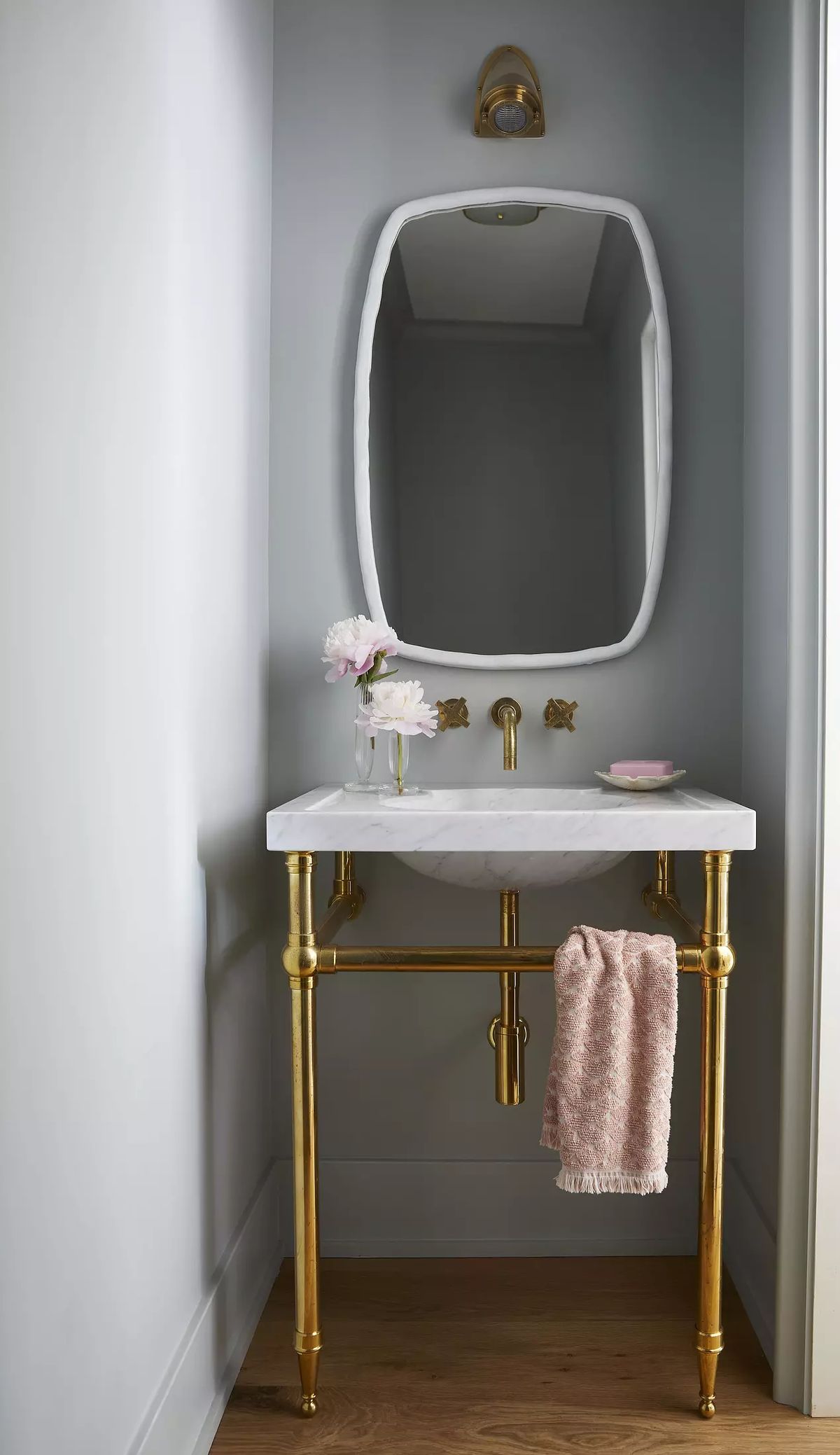 Powder room with marble sink, gold base, oval mirror, wall sconce, and pink towel.