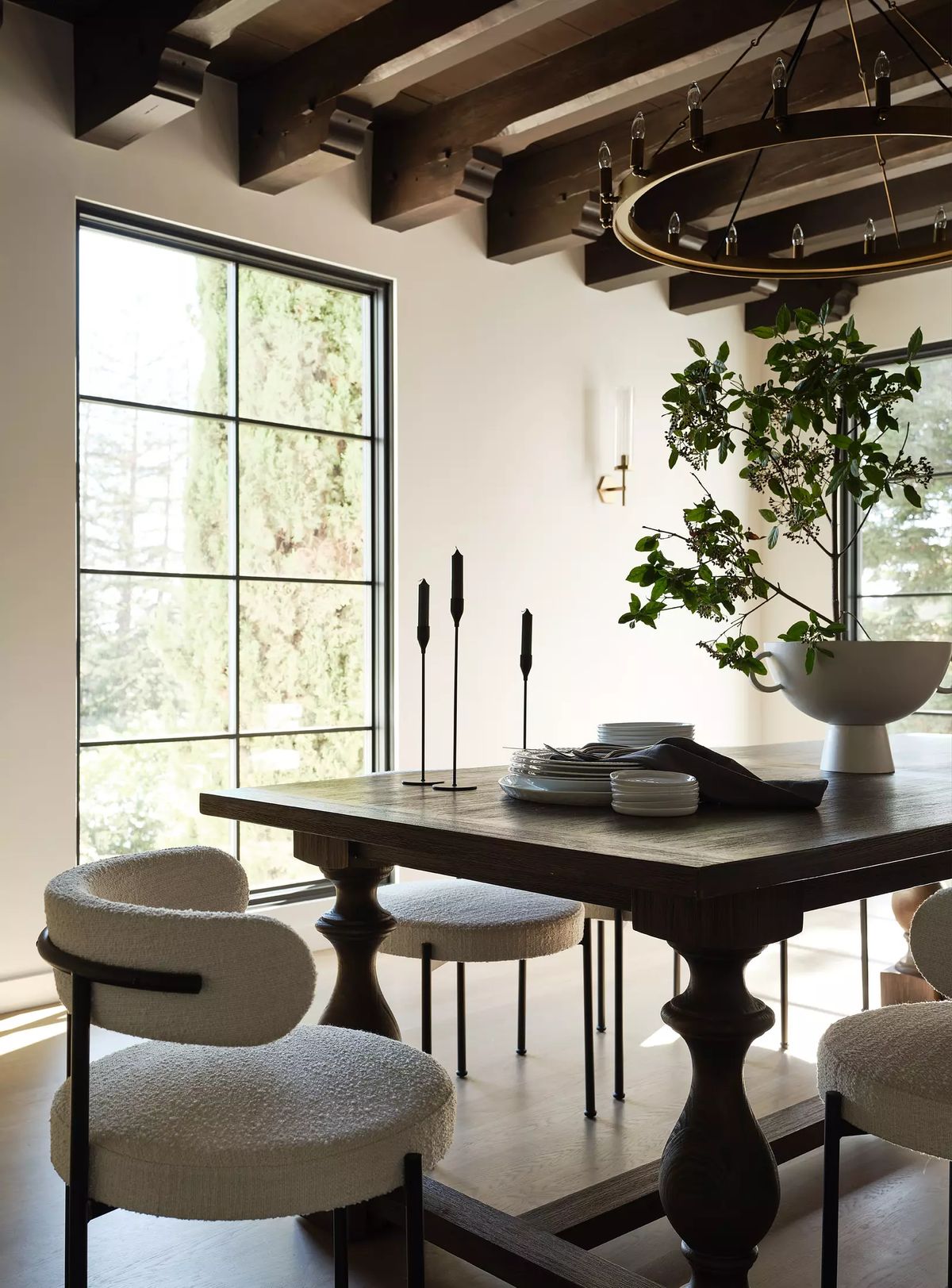 Dining room with wooden table, padded chairs, decorative centerpiece, and large windows with exposed beams