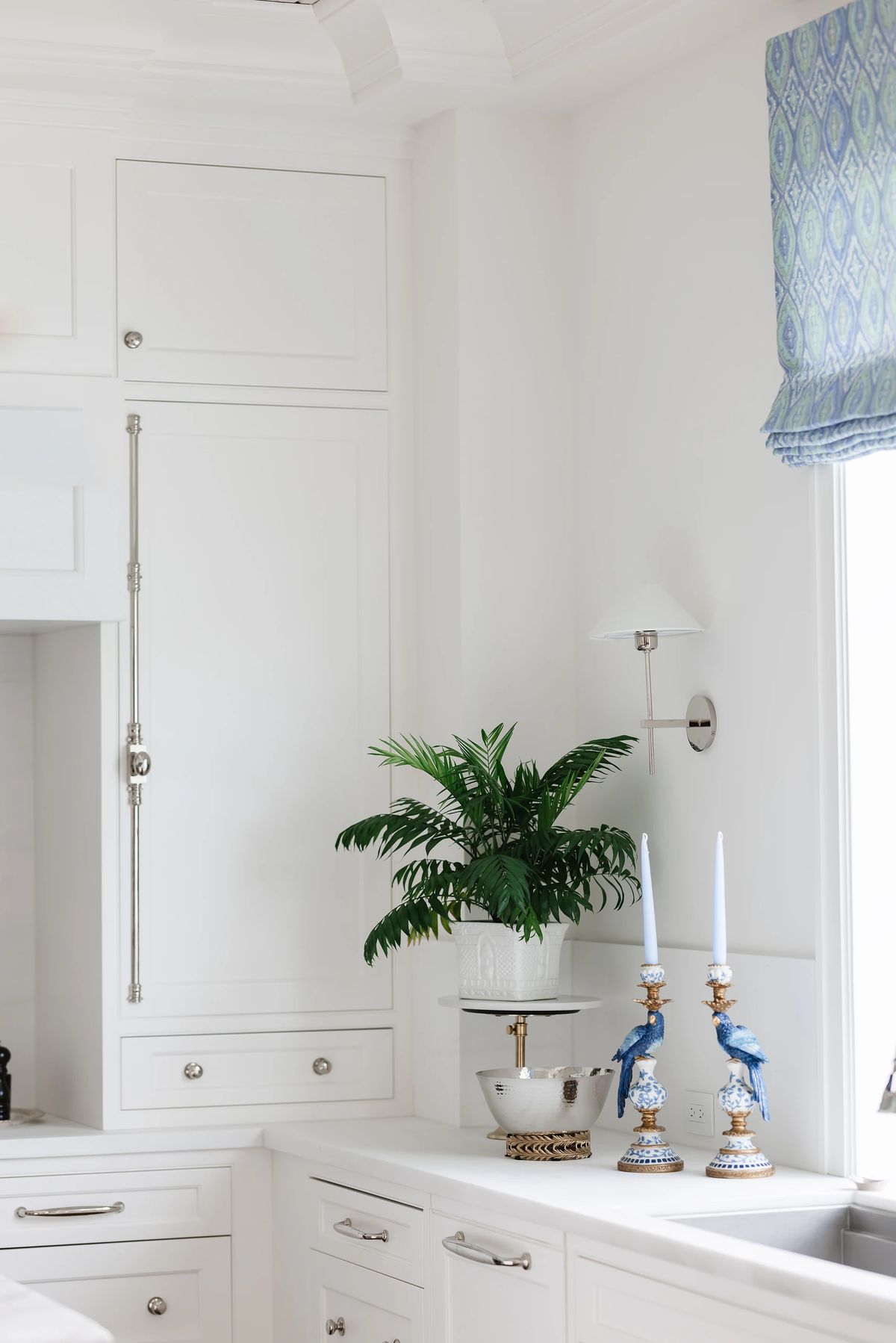 Kitchen with white cabinetry, countertop decor, blue-patterned valance, and a wall-mounted light fixture.