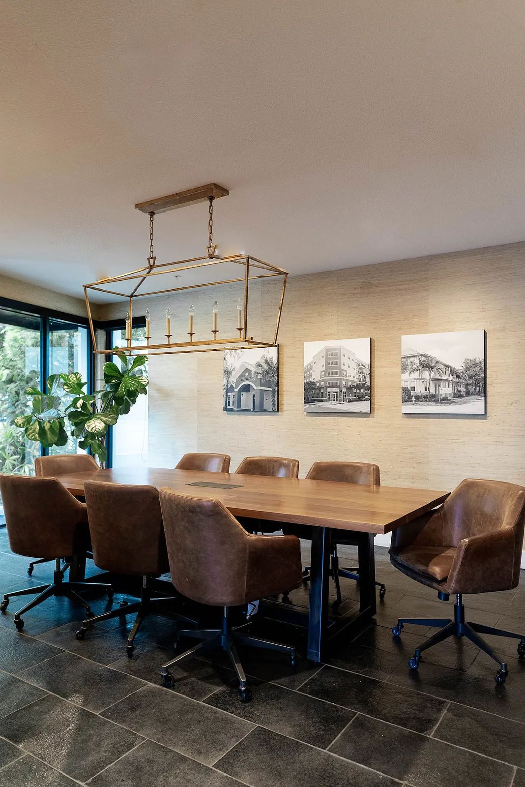 Dining room with large wooden table, brown chairs, framed photos, and glass door to outdoor view