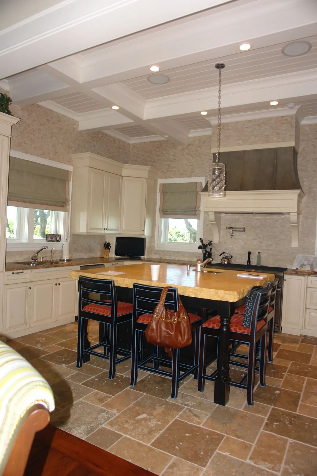 Kitchen with large island, white cabinets, stone tile flooring, and dual windows for natural light.