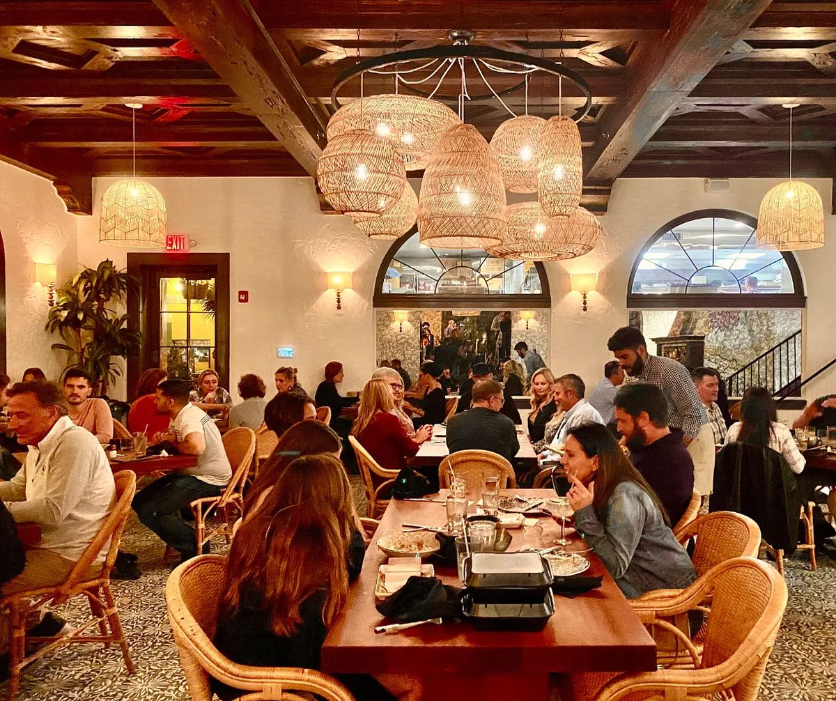 Dining room with wooden tables, woven chairs, pendant lights, and arched windows.