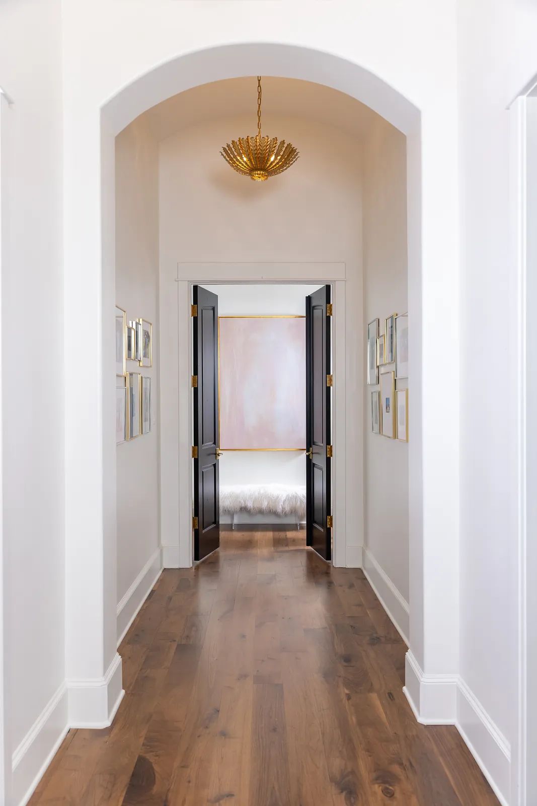 Hallway with black double doors, white walls, framed artworks, and wooden floor.