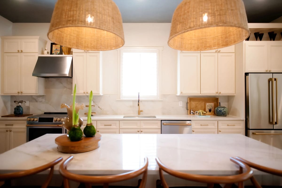 Kitchen with white cabinetry, marble island, stainless steel appliances, window, and pendant lights.