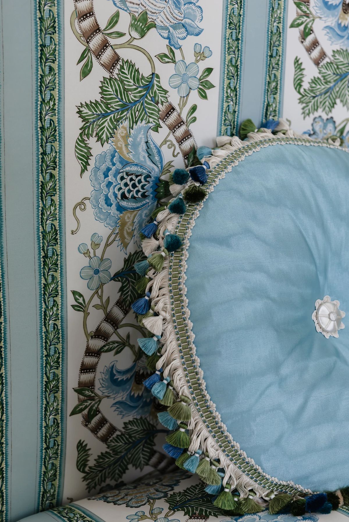 Close-up of embroidered fabric with floral patterns and tufted cushion in blue and green shades.