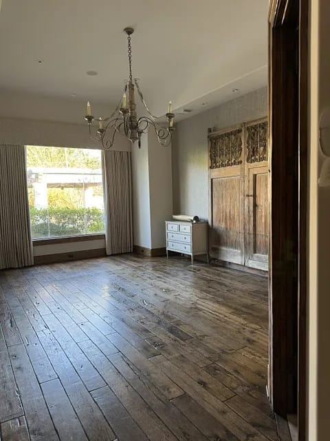 Living room with wooden floor, large window, sideboard, and chandelier.