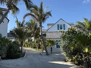 Exterior front view of a house with white siding, blue shutters, palm trees, and a sandy path.