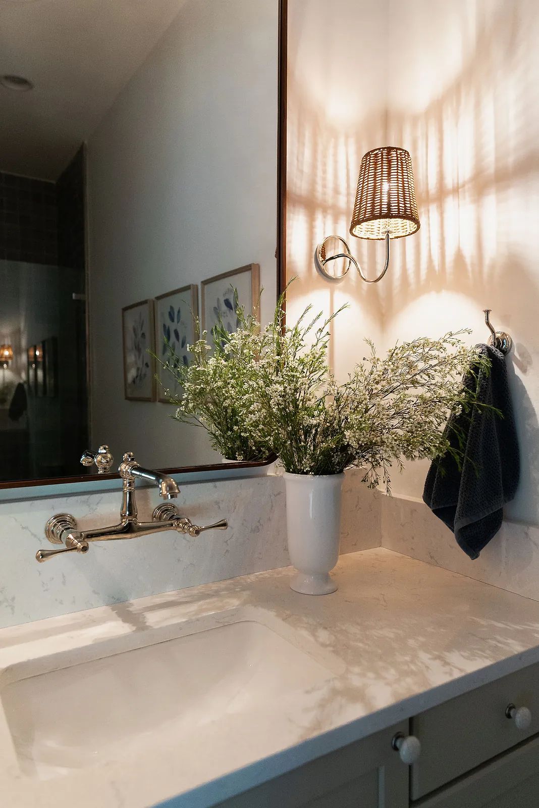 Bathroom with white sink, silver faucet, marble countertop, greenery, and a glass shower enclosure.