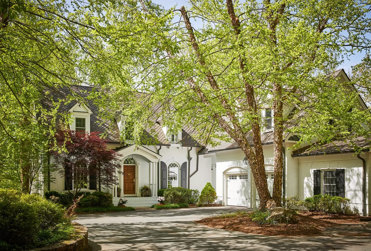 Exterior front view of a house with white siding, arched entrance, and driveway leading to a garage.