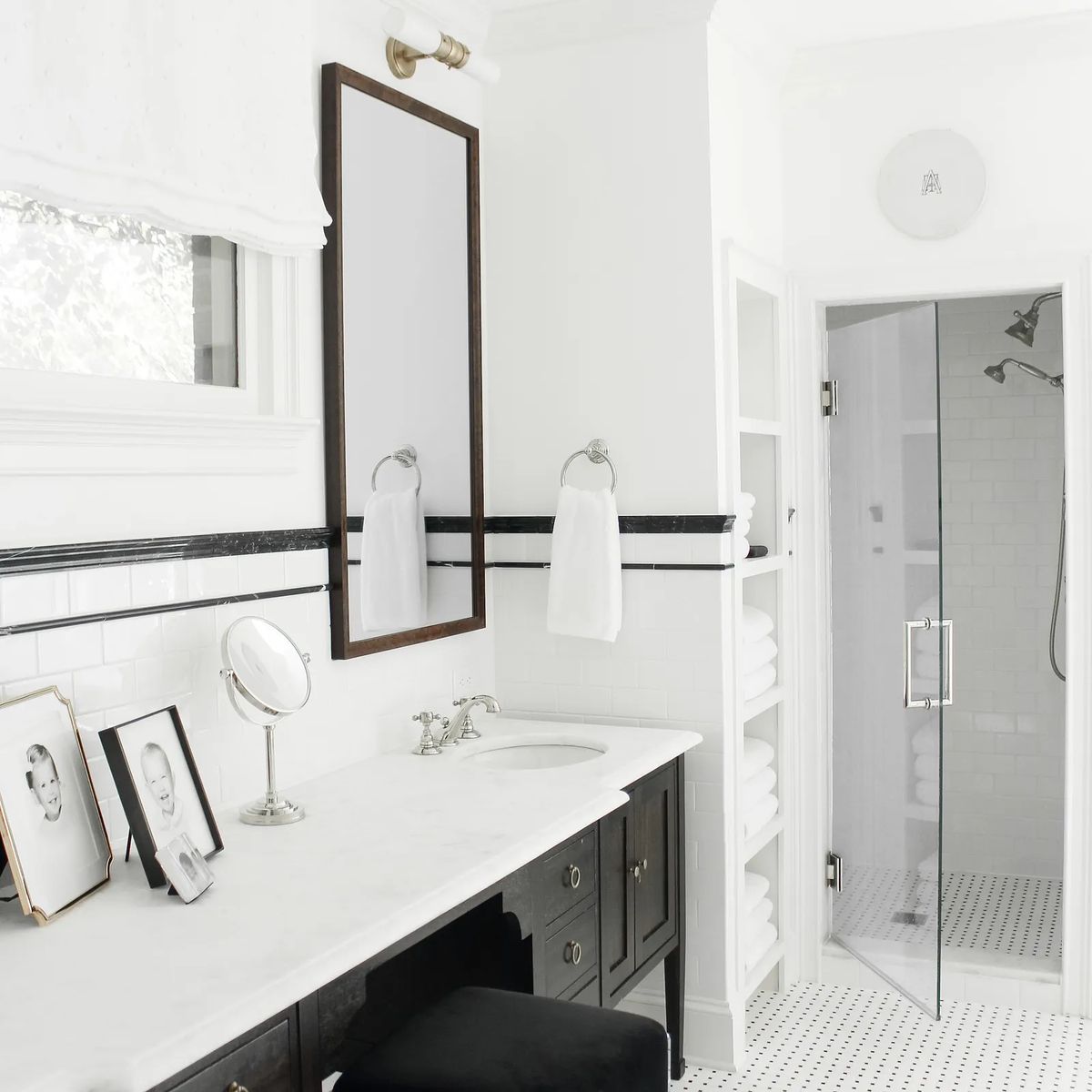 Bathroom with double sink vanity, marble countertop, large mirror, glass shower, framed photos, and stacked towels.