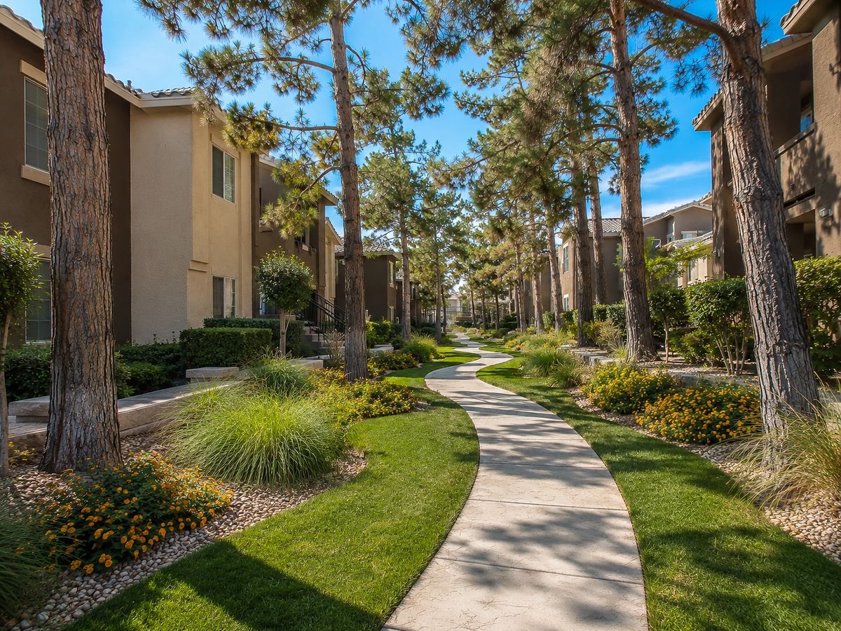 Garden path with trees, shrubs, and flower beds alongside a concrete walkway.
