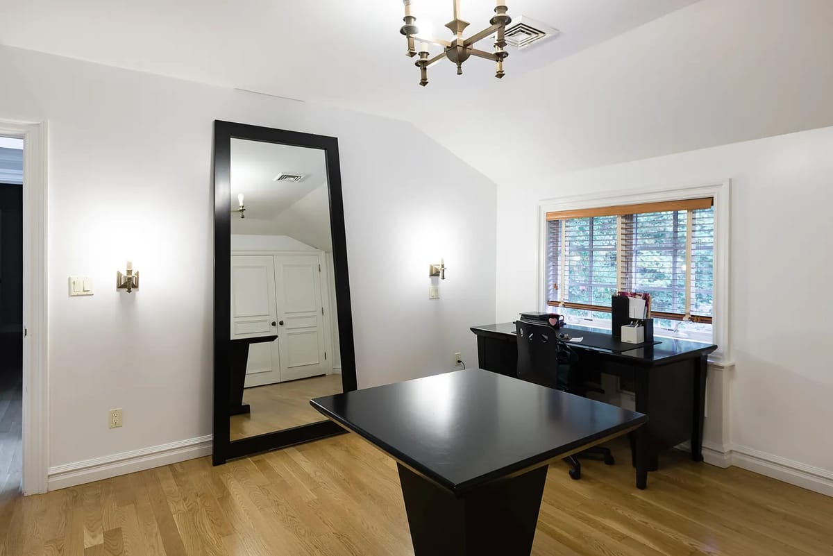 Office with black desk, large mirror, desk chair, window with blinds, and wall sconces.