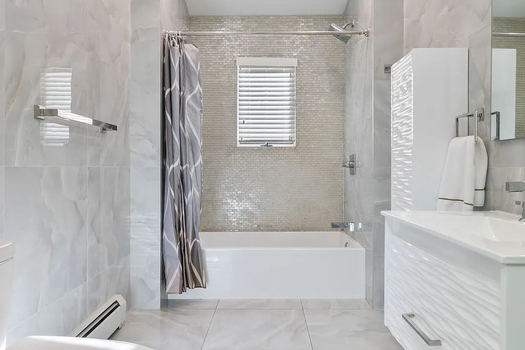 Bathroom with white bathtub, textured vanity, mosaic tile accent, and window with natural light