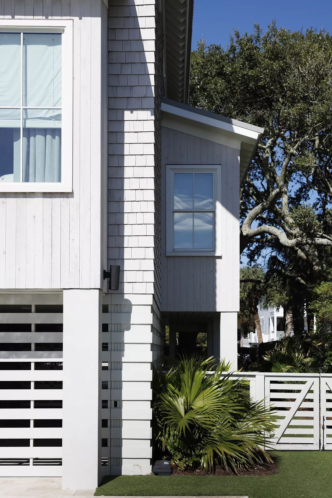 Exterior front of a building with wood siding, windows, palm tree, and grass.