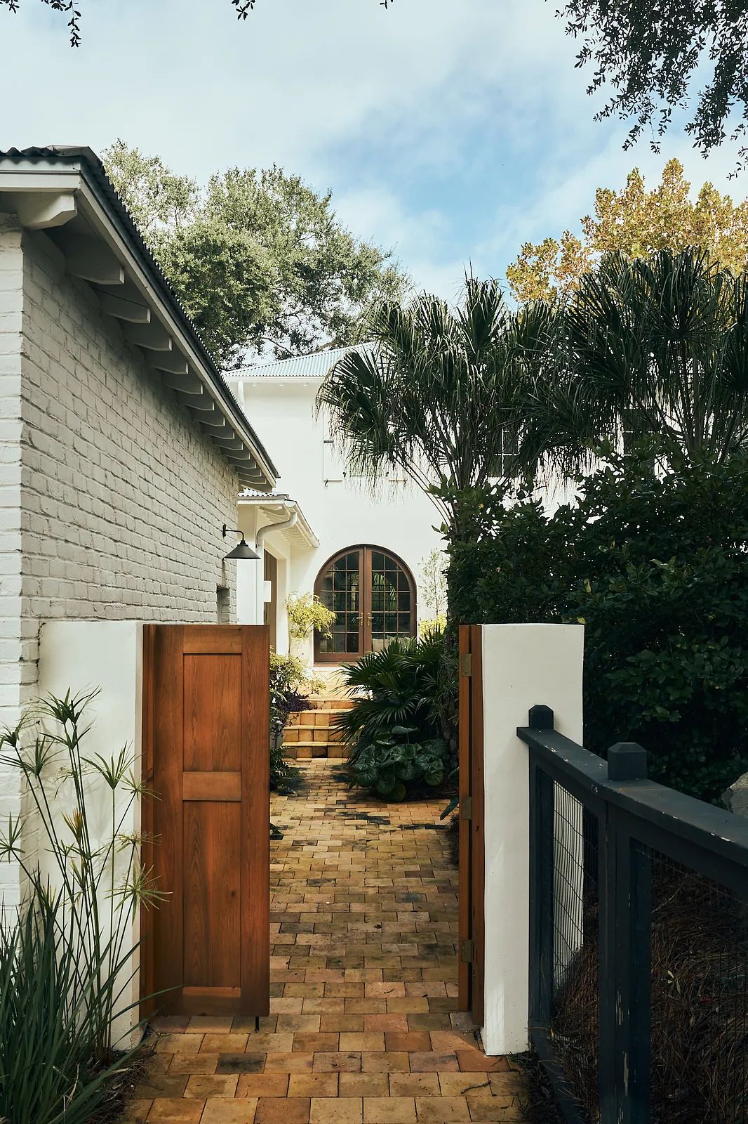 Exterior front area with brick pathway, arched door, plants, and wooden gates.