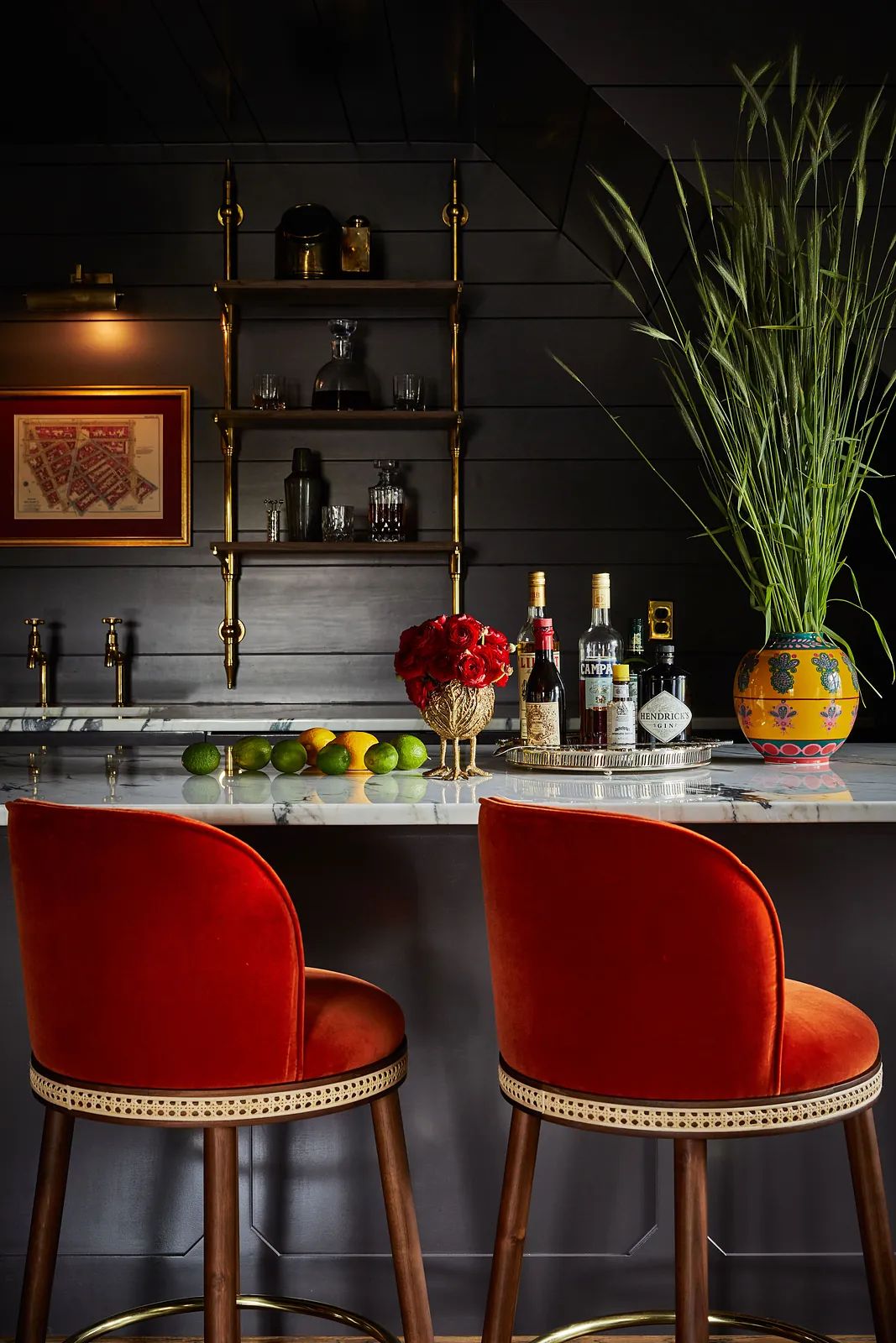 Bar area with red stools, marble countertop, shelving with glassware, and decorative items including fruits and greenery.