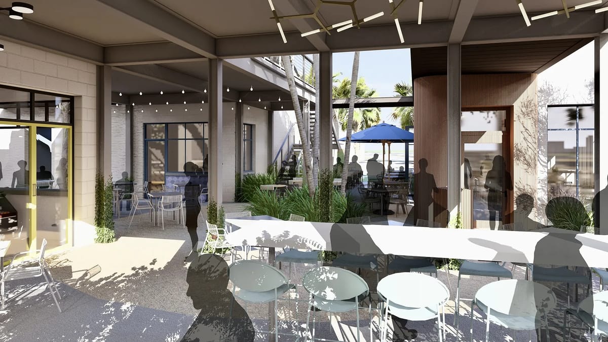Outdoor patio with white table, blue chairs, plants, and large umbrella, connecting to an indoor area.