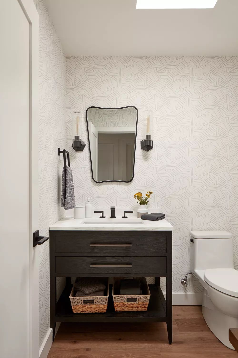 Bathroom with black vanity, white countertop, large mirror, wall sconces, and wooden floor