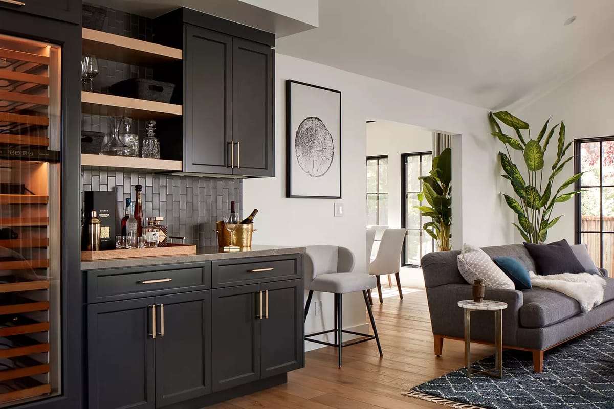Living room with gray sofa, side table, dark cabinet, wall art, large window, and leafy plant.
