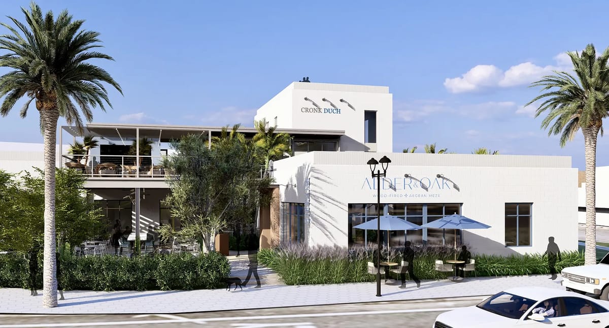 Exterior view of a modern building with a patio, large windows, and palm trees.