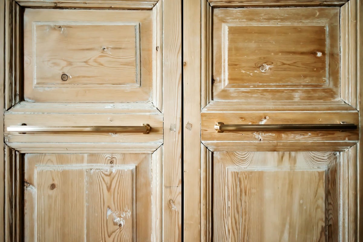 Wooden doors with natural finish, flat panels, brass handles, and visible grain texture.
