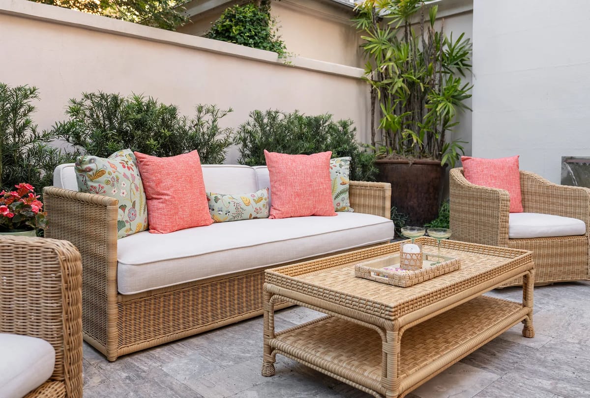 Patio with woven rattan sofa, chairs, wicker coffee table, and surrounding potted plants.