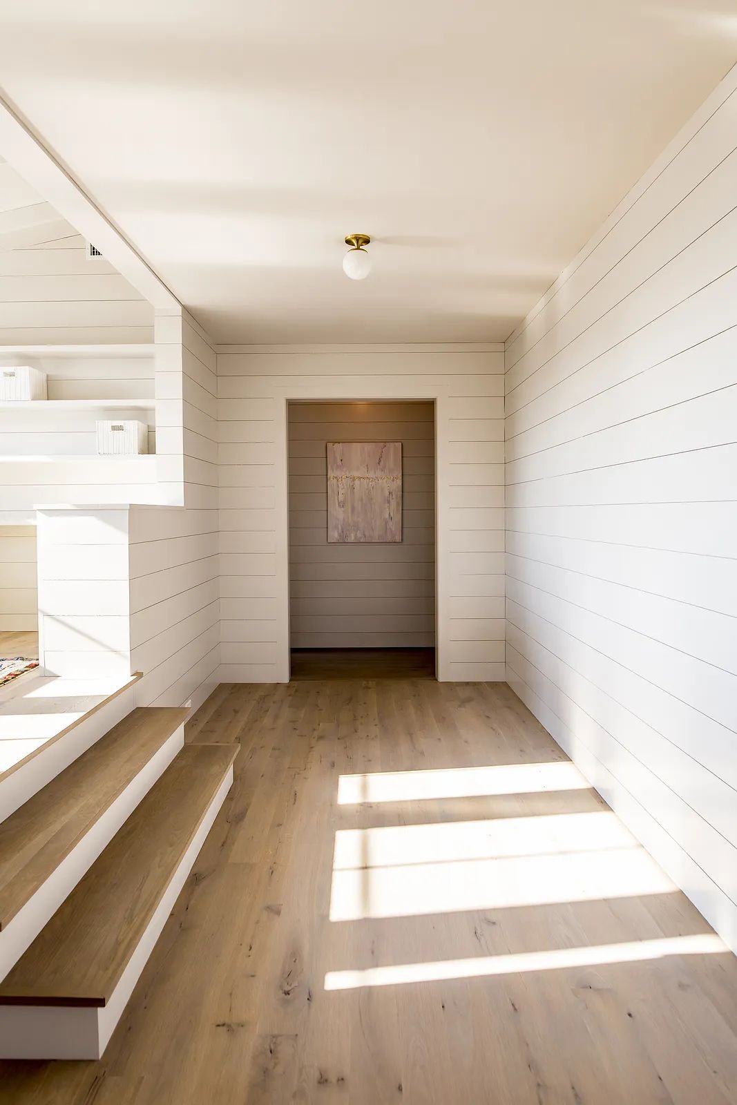 Foyer with light wood flooring, white shiplap walls, staircase, and artwork on the wall.