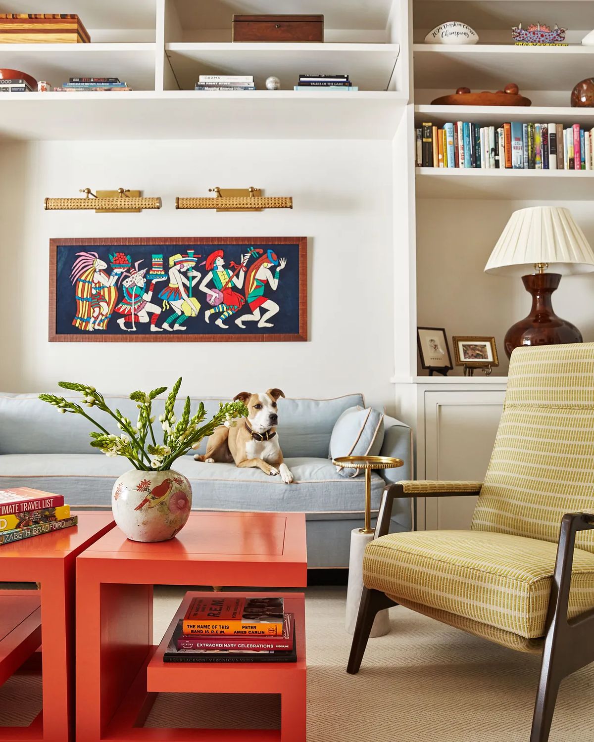Living room with blue sofa, red coffee table, patterned armchair, bookshelves, and dog.