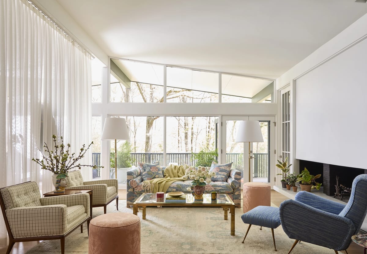 Living room with blue sofa, coffee table, armchairs, fireplace, and large windows with sheer curtains.