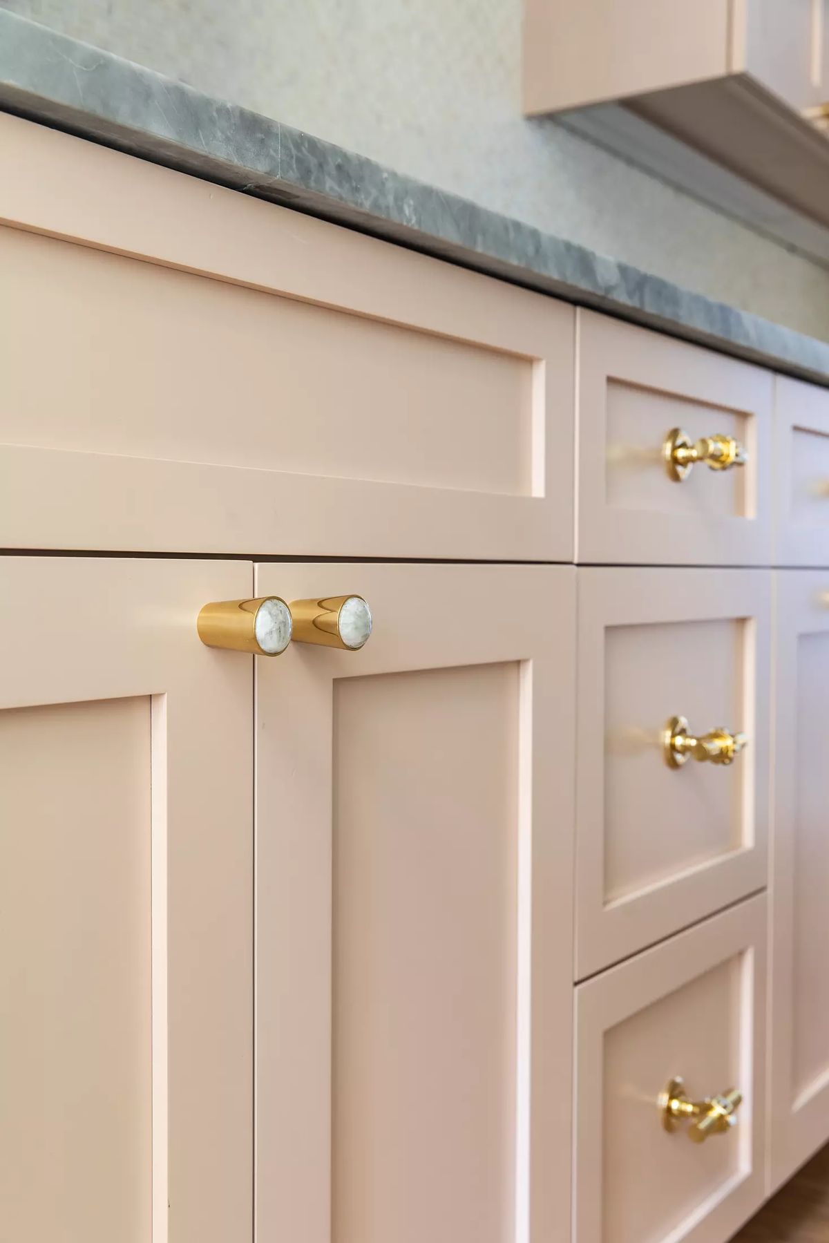 Kitchen with pink cabinets, gray countertop, gold hardware, and flat panel doors.