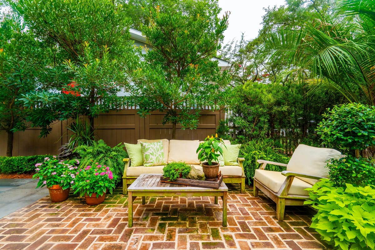 Garden seating area with two sofas, wooden table, potted plants, and lush greenery.