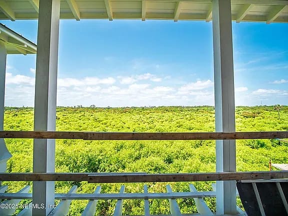 Open patio with wooden railings, flooring, white columns, and expansive views of greenery under a blue sky.