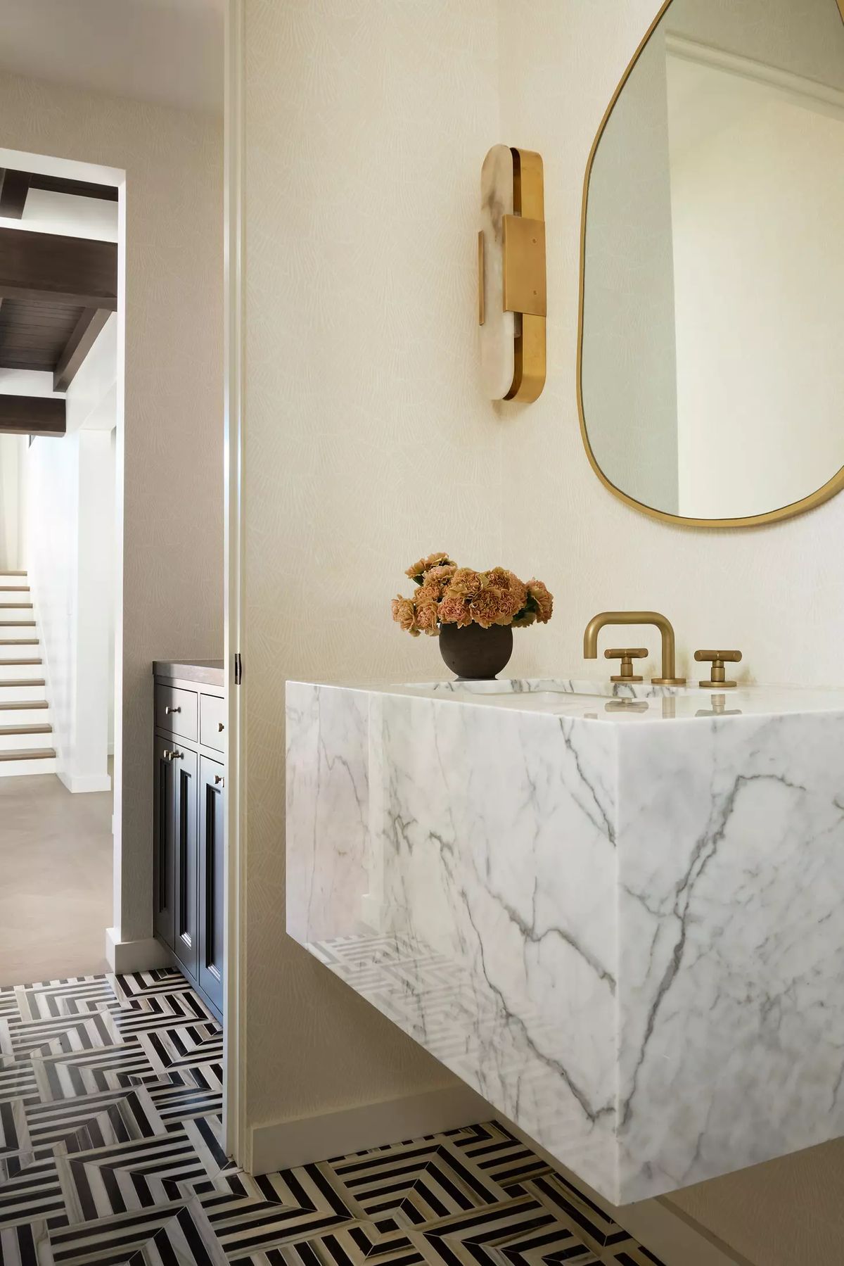 Bathroom with wall-mounted marble sink, gold faucets, round mirror, and geometric floor tiles.