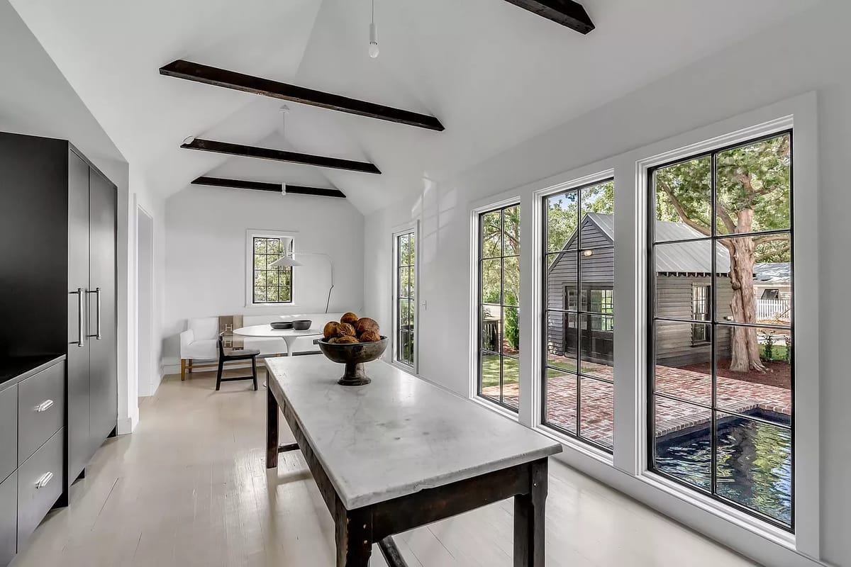 Kitchen with marble-topped island, black cabinetry, white sofa, and large windows overlooking garden.
