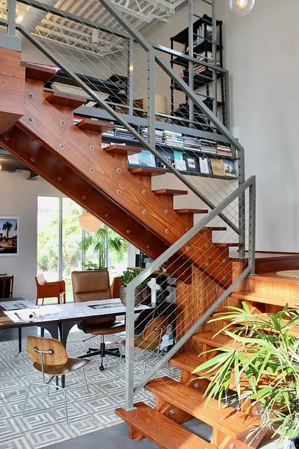 Office space with wooden staircase, desk, leather chair, bookshelves, and decorative plant.
