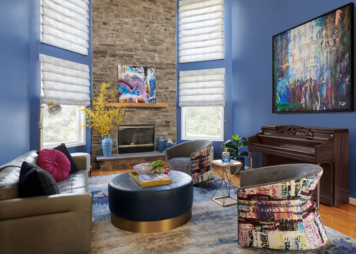 Living room with brown leather sofa, colorful chairs, blue coffee table, stone fireplace, and grand piano.