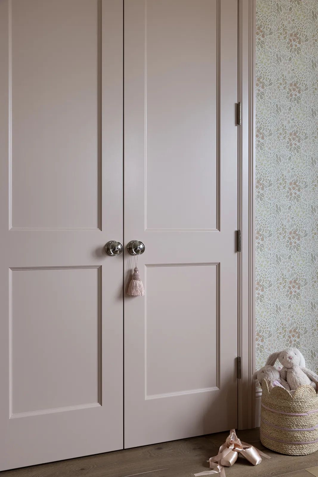 Corner with pink doors, floral wallpaper, and a basket holding a stuffed animal.