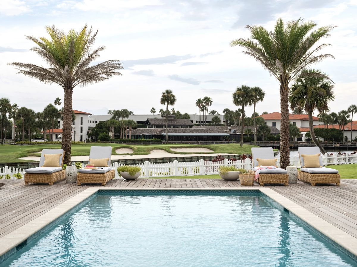 Outdoor patio with swimming pool, lounge chairs, side tables, palm trees, and golf course view.