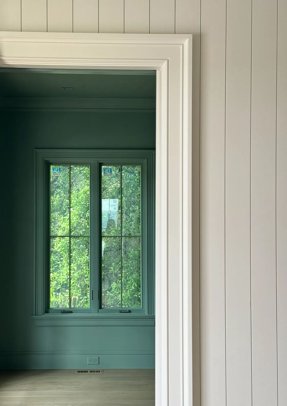 Room with light blue walls and a white trim, featuring a large window with greenery outside.