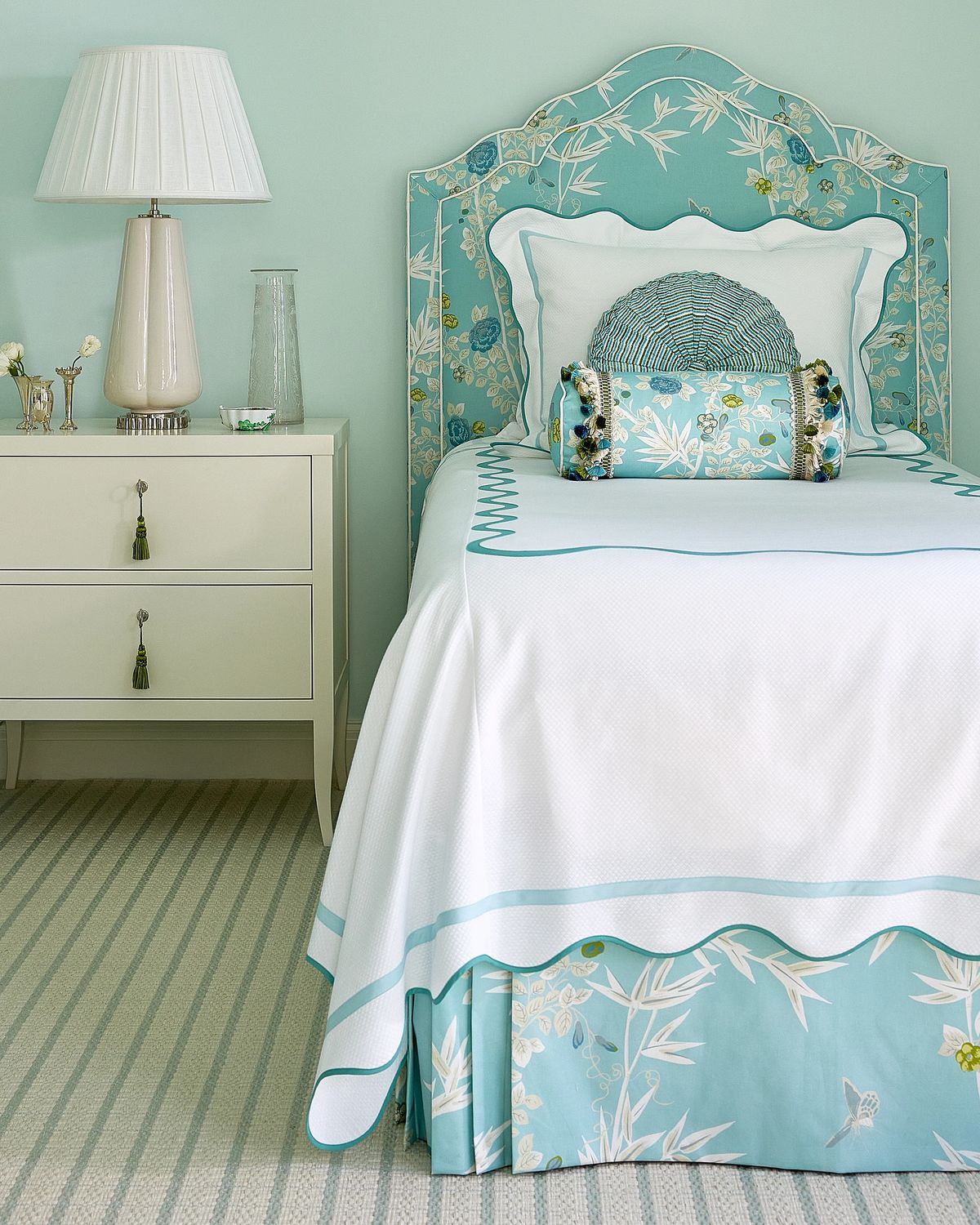 Bedroom with decorative headboard bed, nightstand, lamp, and striped rug.